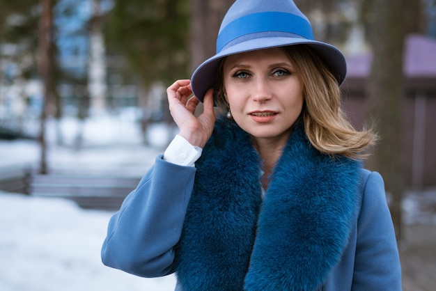 Bella donna con il trucco, in un cappotto blu e un cappello, in posa nella natura sulla neve