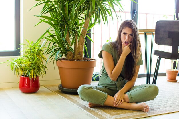 Bella donna con la bocca e gli occhi spalancati e la mano sul mento, che si sente spiacevolmente scioccata, dice cosa o wow