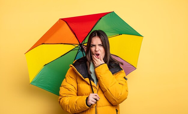 Bella donna con la bocca e gli occhi spalancati e la mano sul mento inverno e concetto di ombrello