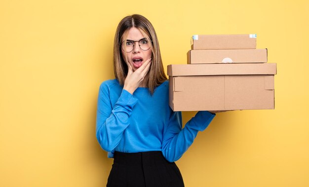 Bella donna con la bocca e gli occhi spalancati e la mano sul mento pacchetti scatole concetto