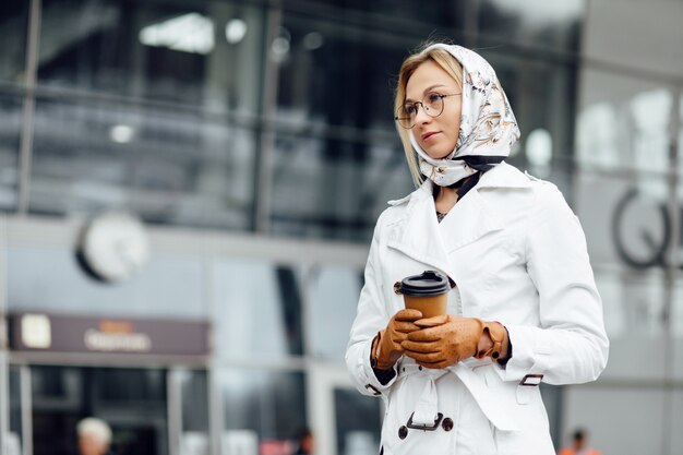 Bella donna con la tazza di caffè vicino all'edificio per uffici.