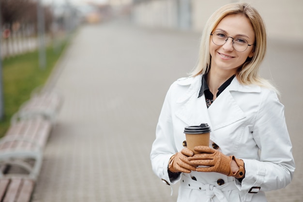 Bella donna con la tazza di caffè vicino all'edificio per uffici.