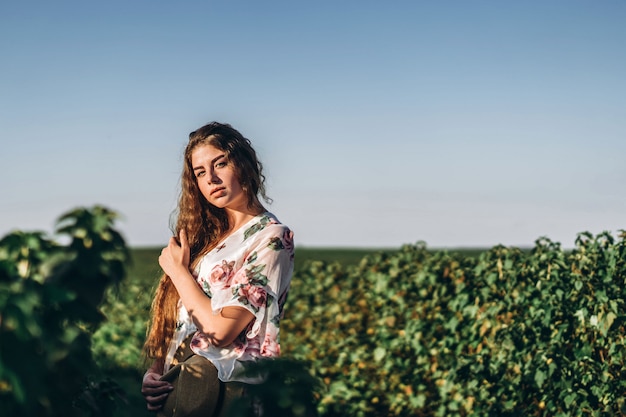 Bella donna con lunghi capelli ricci e lentiggini faccia sul campo di ribes. La ragazza in un vestito chiaro cammina nel giorno soleggiato dell'estate