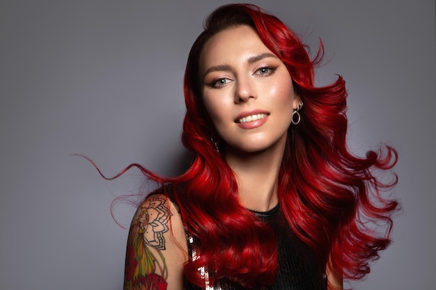 Bella donna con lunghi capelli rossi ondulati Sfondo grigio piatto Donna con tatuaggio