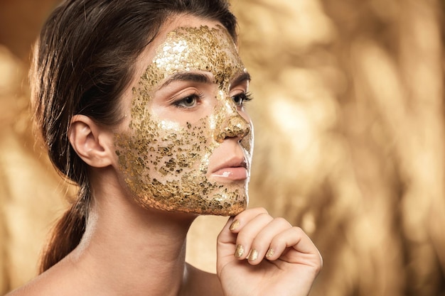 Bella donna con maschera dorata brillante sul viso per il trattamento della pelle