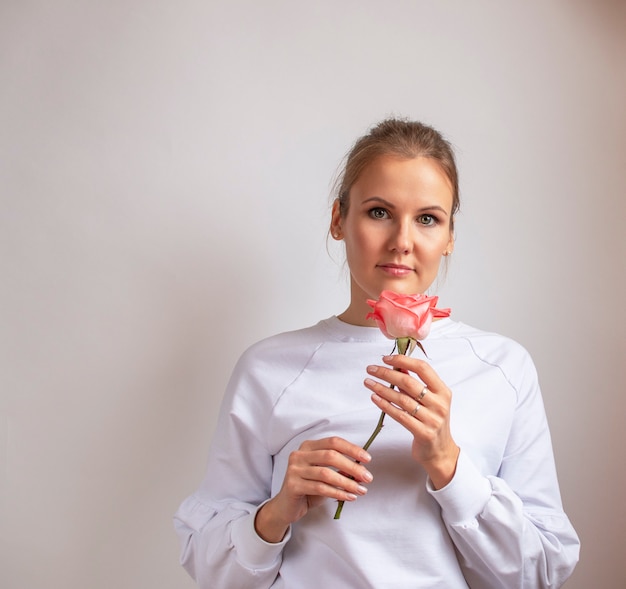 Bella donna con rosa. Ragazza in una giacca bianca con un fiore tra le mani