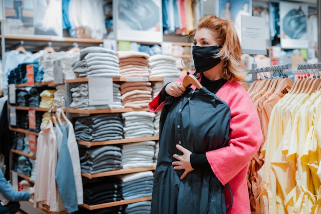 Bella donna con telefono cappotto rosa brillante shopping Mall con maschera protettiva nera sul viso