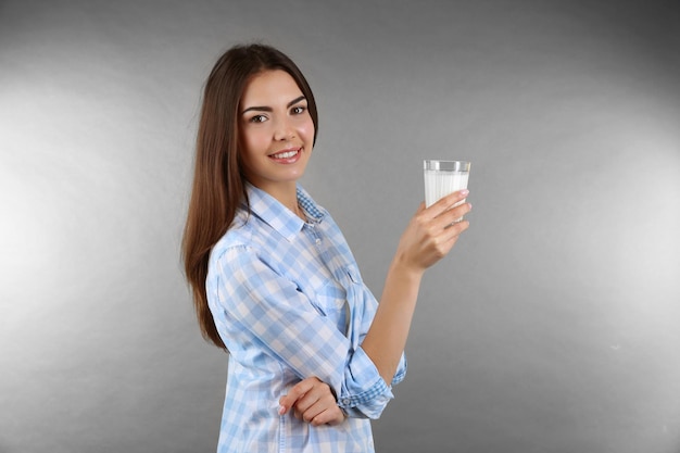 Bella donna con un bicchiere di latte su sfondo grigio