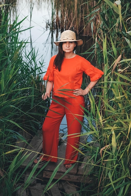 Bella donna con un cappello di paglia vestito con abiti rossi su uno sfondo di canne e lago
