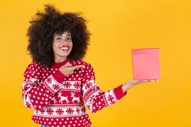 Bella donna con un maglione natalizio e un regalo nelle sue mani, sfondo giallo