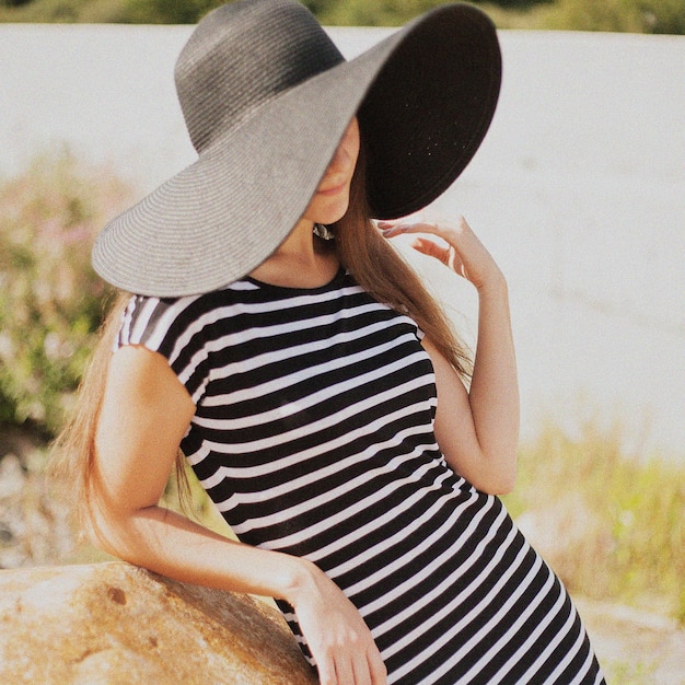 Bella donna con un vestito a righe e un cappello nero.