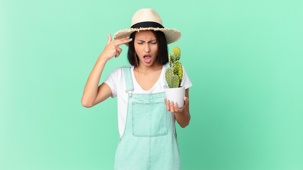 Bella donna contadina che sembra infelice e stressata, gesto suicida che fa il segno della pistola e tiene in mano un cactus