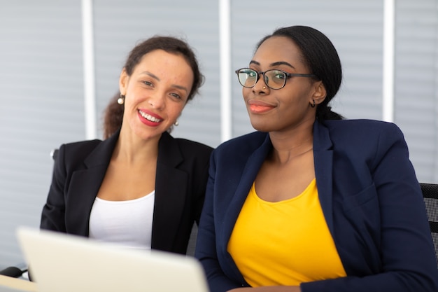 Bella donna d'affari afroamericana e ispanica che lavora insieme al computer portatile al moderno ufficio a casa.