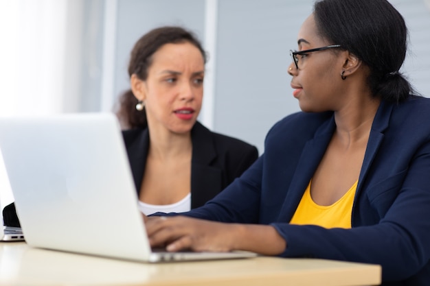 Bella donna d'affari afroamericana e ispanica che lavora insieme al computer portatile al moderno ufficio a casa.