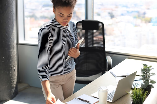 Bella donna d'affari afroamericana in abbigliamento casual intelligente che lavora al computer portatile in ufficio.