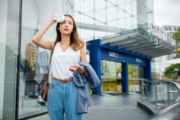 Bella donna d'affari asiatica che si asciuga il sudore sul viso con un panno nella calda giornata estiva con tempo caldo, donna che ha danni alla pelle da insolazione da sole UV città inquinamento atmosferico all'aperto sulla strada