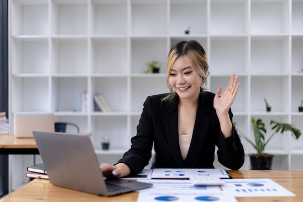 Bella donna d'affari asiatica seduta nel suo ufficio privato, sta parlando con il suo partner tramite videochiamata sul suo laptop, è una dirigente donna di una startup. Concetto di gestione finanziaria