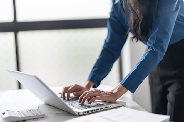 Bella donna d'affari asiatica sicura di sé che lavora con il portatile con le mani che digitano la tastiera professionale