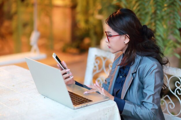 bella donna d'affari con gli occhiali controllando il cellulare mentre si lavora sul computer