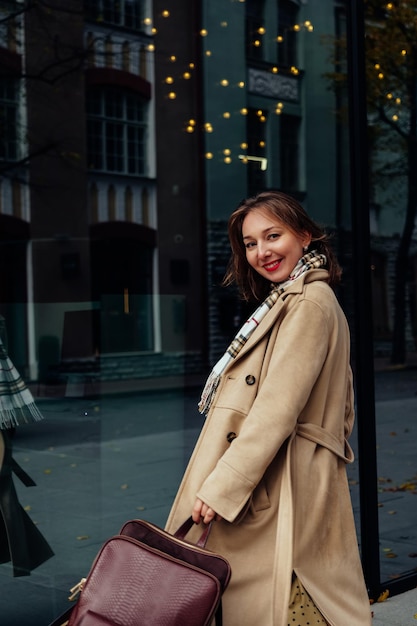 Bella donna d'affari felice che indossa un cappotto beige che cammina in città con uno zaino in pelle