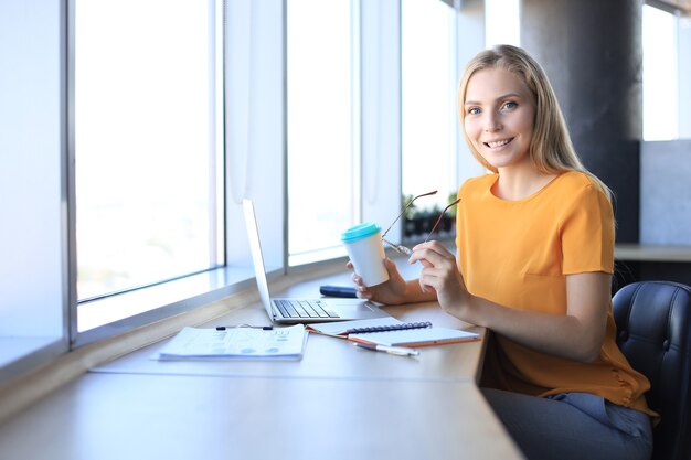 Bella donna d'affari in abbigliamento casual intelligente che lavora al computer portatile in ufficio.