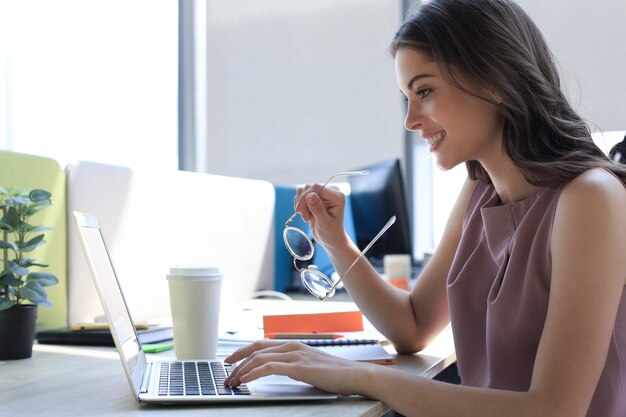 Bella donna d'affari in abbigliamento casual intelligente che lavora al computer portatile in ufficio.