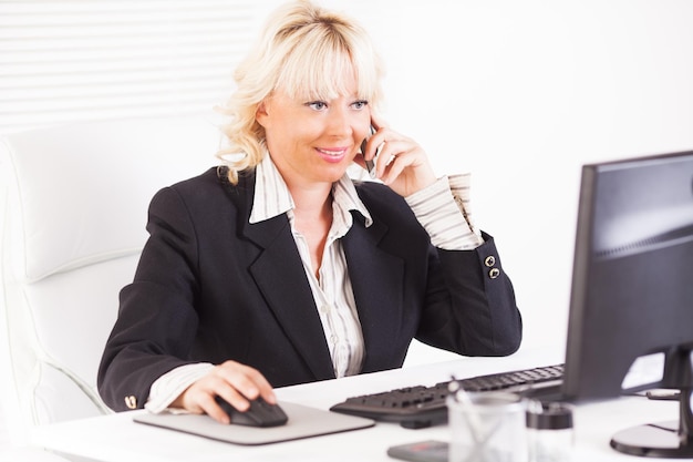 Bella donna d'affari matura parlando sul telefono cellulare sul posto di lavoro.