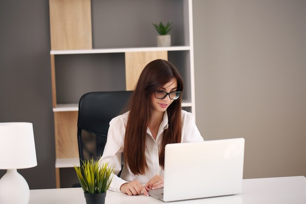 Bella donna d'affari utilizza un laptop e sorride mentre si lavora in ufficio.