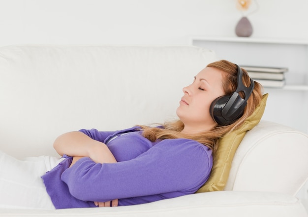 Bella donna dai capelli rossi che ascolta la musica mentre si riposa sdraiata su un divano