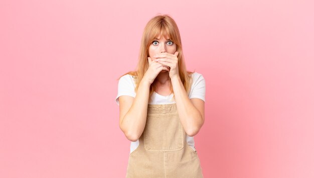 bella donna dai capelli rossi che copre la bocca con le mani con uno shock