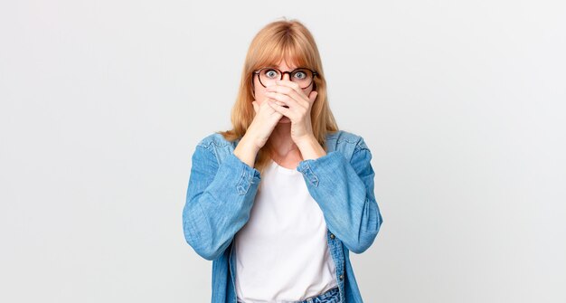 Bella donna dai capelli rossi che copre la bocca con le mani con uno shock