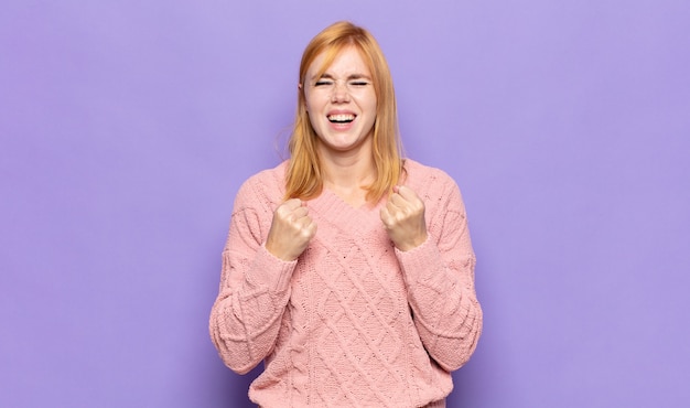 Bella donna dai capelli rossi che grida trionfalmente, ride e si sente felice ed eccitata mentre celebra il successo