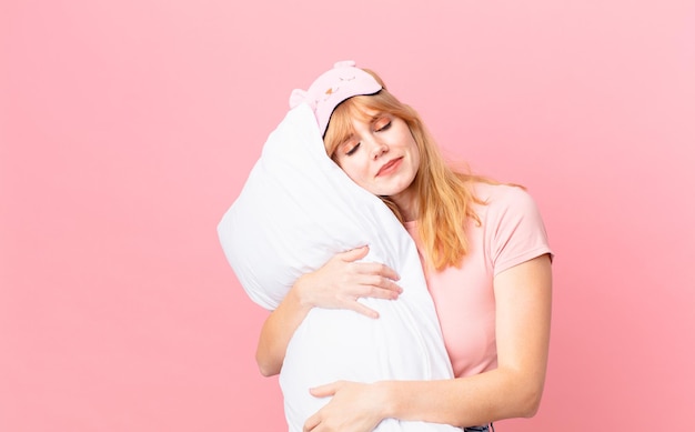 Bella donna dai capelli rossi che indossa un pigiama e tiene un cuscino