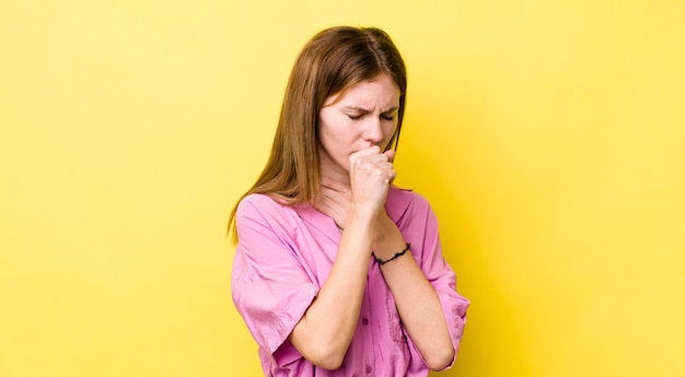 Bella donna dai capelli rossi che si sente male con mal di gola e sintomi influenzali che tosse con la bocca coperta