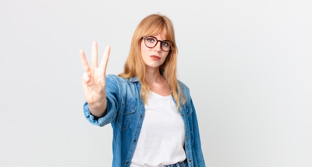 Bella donna dai capelli rossi che sorride e sembra amichevole, mostrando il numero tre