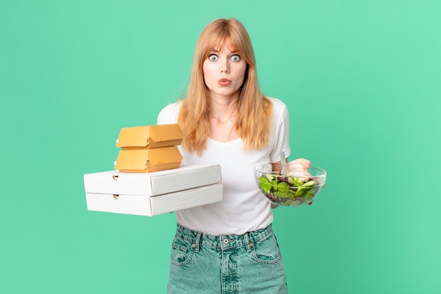 Bella donna dai capelli rossi che tiene in mano scatole di fast food e un'insalata?