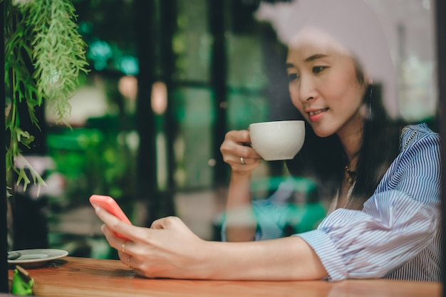 Bella donna dell&#39;Asia che utilizza telefono cellulare e che beve caffè nella caffetteria in vacanza