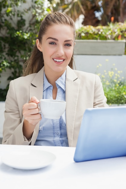 Bella donna di affari che mangia un caffè facendo uso della compressa