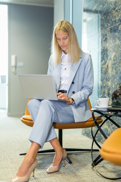 Bella donna di affari che si siede alla tavola che lavora ad una donna alla moda del computer portatile nell'ufficio moderno