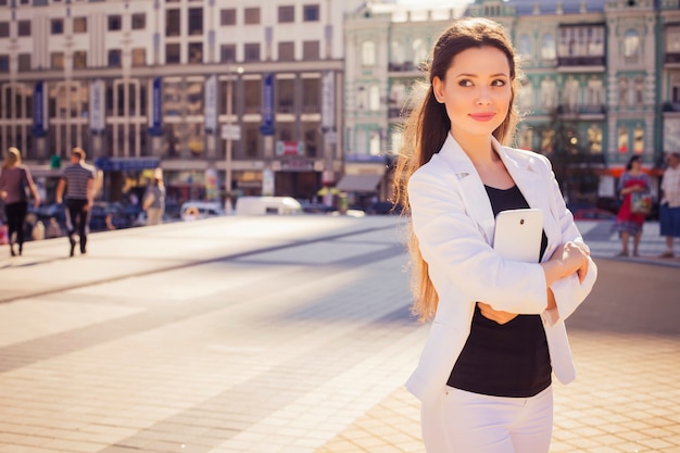 Bella donna di affari del brunette in vestito bianco che lavora ad un ridurre in pani in sue mani all'aperto. copia spazio