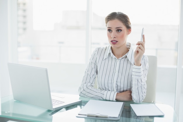 Bella donna di affari di pensiero che tiene una penna che si siede al suo scrittorio