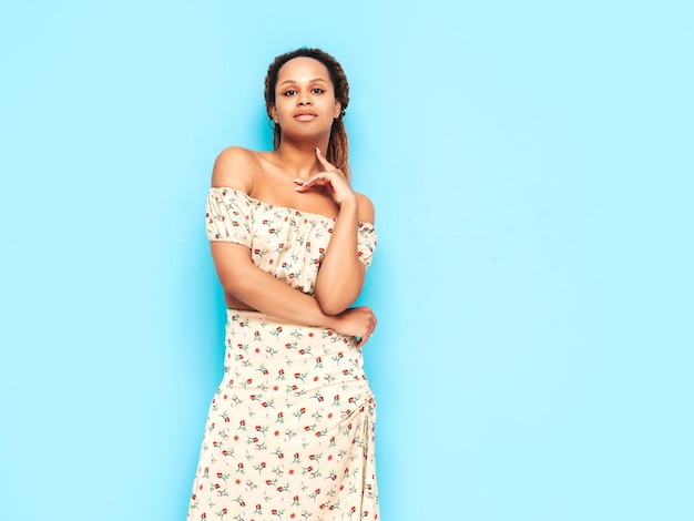 Bella donna di colore con l'acconciatura di riccioli afro Modello sorridente vestito in abito estivo Femmina spensierata sexy in posa vicino al muro blu in studio Abbronzato e allegro