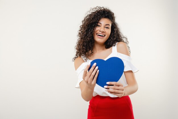 Bella donna di colore con la carta del biglietto di S. Valentino a forma di cuore blu isolata