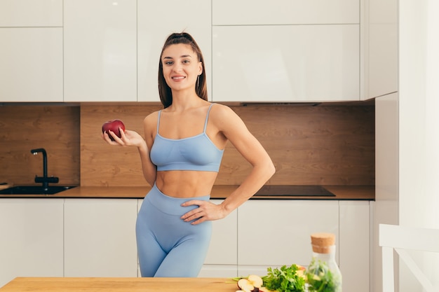 Bella donna di forma fisica che prepara cibo sano a casa, tenendo in mano una mela