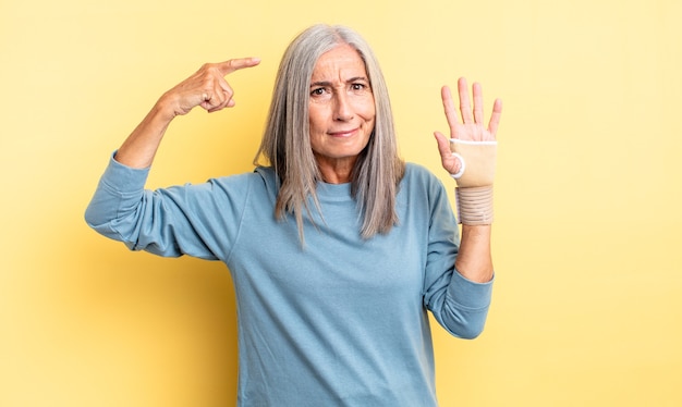 Bella donna di mezza età che si sente confusa e perplessa, mostrando che sei pazzo. concetto di fasciatura per le mani