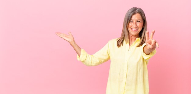 Bella donna di mezza età che sorride e sembra felice, gesticolando vittoria o pace