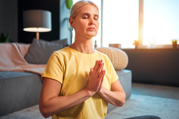 Bella donna di mezza età con gli occhi chiusi che medita stringendo i palmi delle mani davanti a te il saluto namaste nella pratica dello yoga