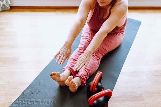 Bella donna di mezza età, modello taglie forti, in top sportivo, seduta su un materassino a casa e facendo yoga,