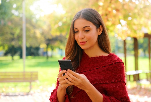 Bella donna di moda di messaggistica con app per smartphone all'aperto autunno inverno stagione.