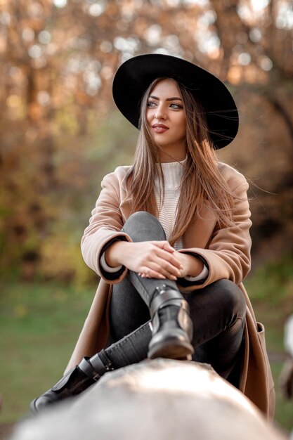 Bella donna di moda in cappello nero che si siede sull'albero